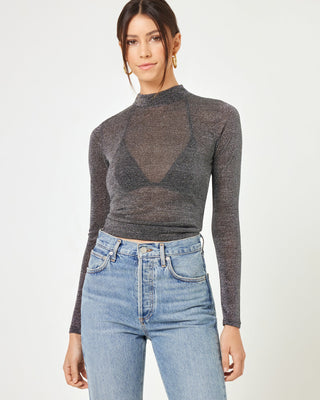 Close-up front view of a model wearing the LSPACE Shimmer Long Sleeve in black, a sheer metallic sparkle mock-neck long-sleeve top with a cropped fit, styled with high-waisted jeans.
