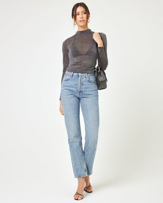 Front view of a model wearing the LSPACE Shimmer Long Sleeve in black, a sheer metallic sparkle mock-neck long-sleeve top, styled with straight-leg jeans and a black shoulder bag.