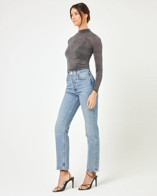 Side view of a model wearing the LSPACE Shimmer Long Sleeve in black, showing the sheer metallic fitted long-sleeve silhouette and mock neckline, styled with straight-leg jeans.