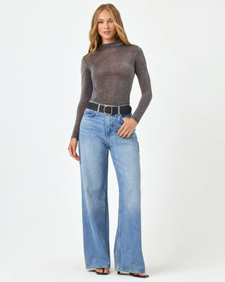 Front view of a model wearing the LSPACE Shimmer Long Sleeve in black, a sheer metallic long-sleeve top with mock neckline and cropped hem, styled with wide-leg jeans and a black belt.